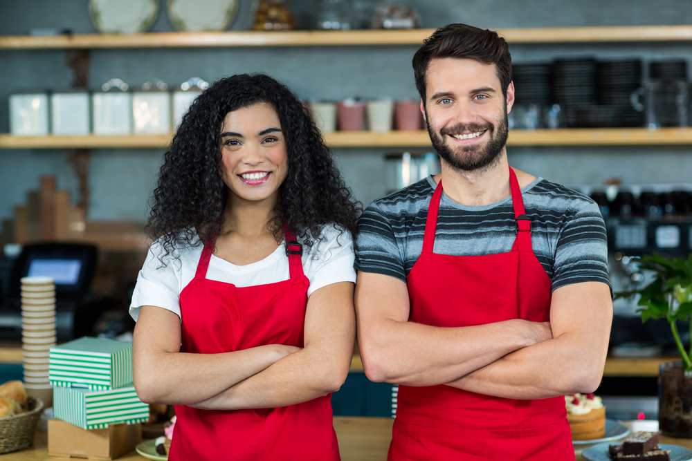 Portrait of smiling waiter and waitress standing at counter in cafe